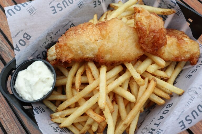 Crispy fried fish fillet atop a mound of golden French fries, accompanied by a small bowl of creamy dipping sauce.