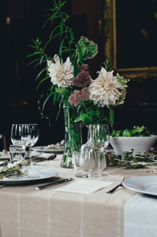 Elegant dining table set with a floral centerpiece, glassware, and a bowl of salad, against a dark, rich backdrop.