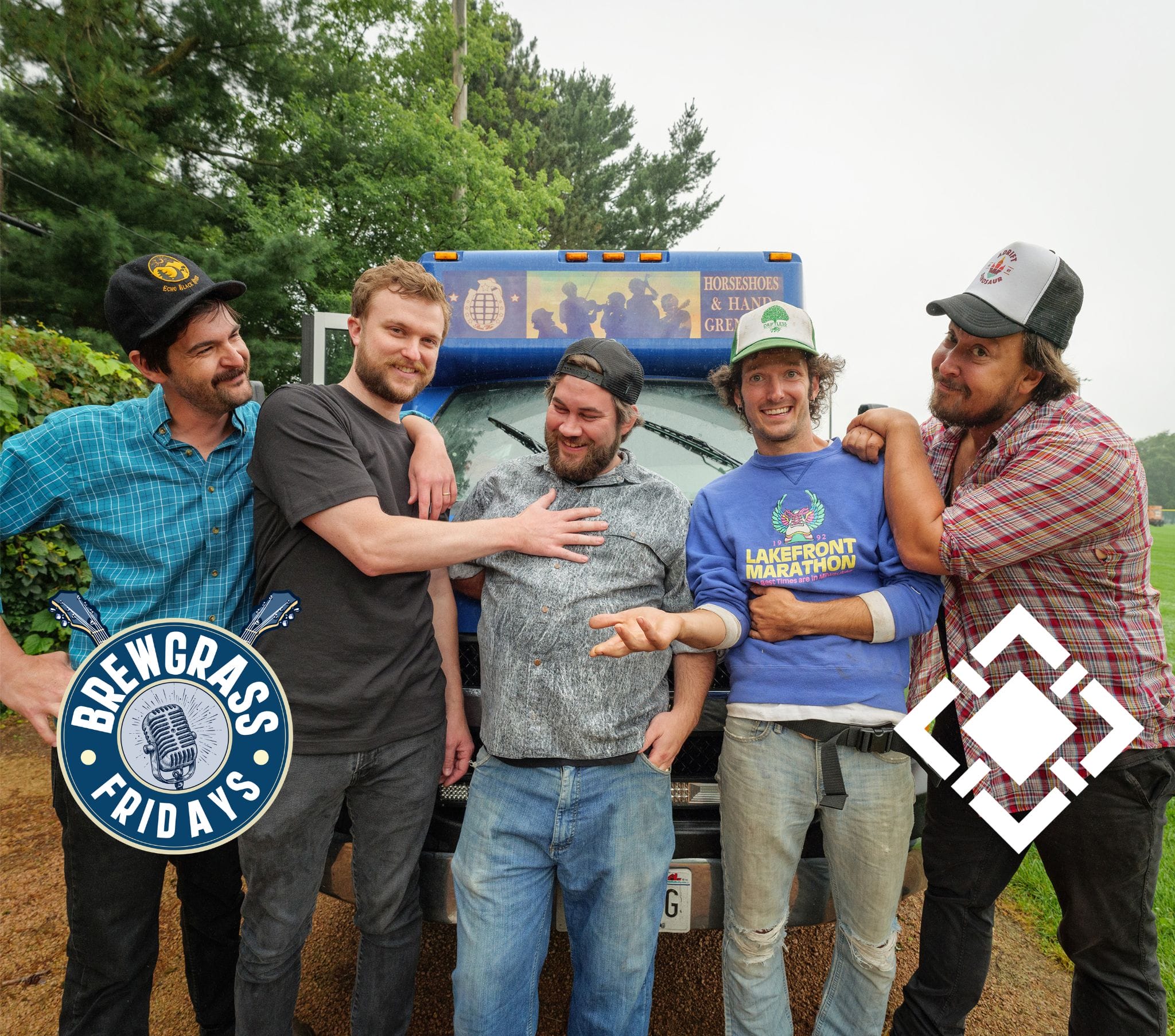 Five men pose playfully in front of a truck, wearing casual clothes and smiling, with greenery in the background.
