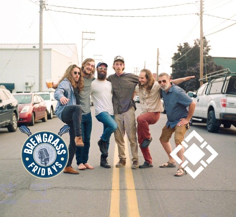 Six men pose playfully on a street, showcasing casual attire and smiles, with cars and buildings in the background.