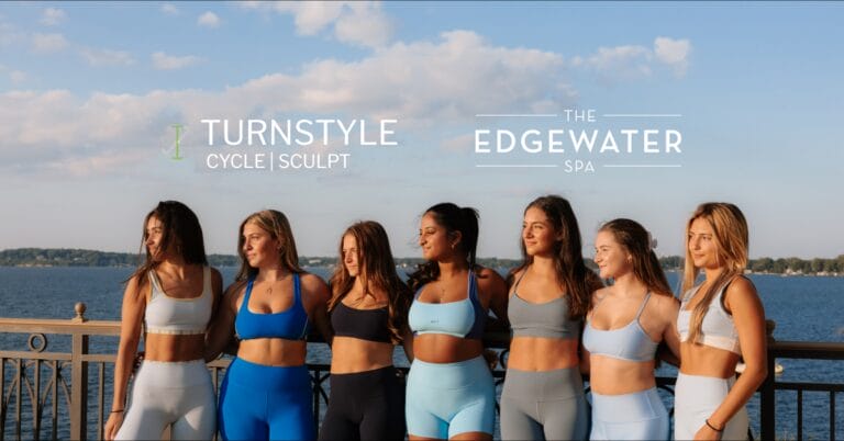 Six women in athletic wear stand by a lake with "Turnstyle Cycle | Sculpt" and "The Edgewater Spa" logos.